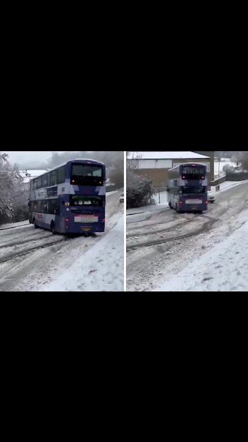 Double decker bus skids in the snow right at another car
