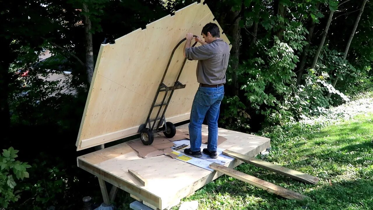 A shed like a plywood box, overhanging a slope.