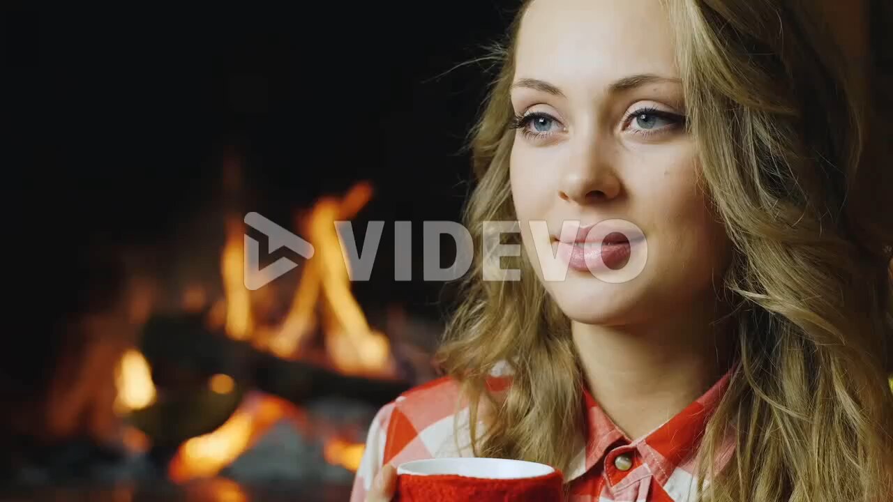 A young woman drinks tea by the burning fireplace