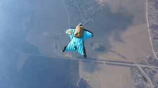 Mand laver wingsuit hop med en rund faldskærm