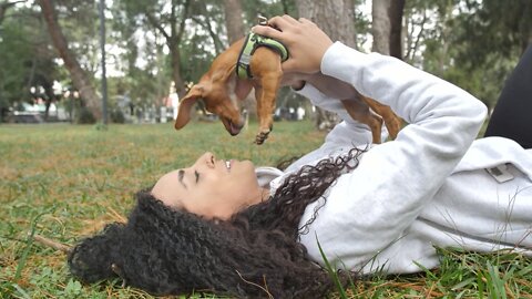 Girl lying on the grass holding her little dog on top.