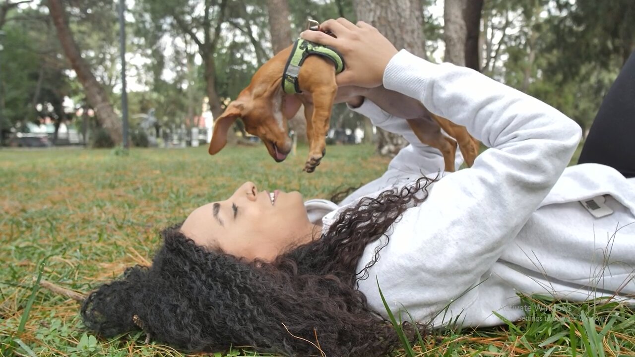 Girl lying on the grass holding her little dog on top.