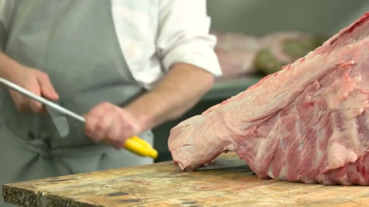 Close up fresh raw meat on table at slaughterhouse Butcher sharpening knife on knife steel in butch