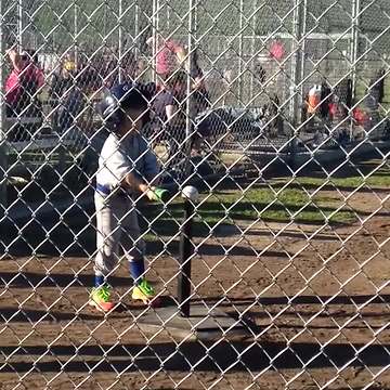 "A tot boy hits a ball off of a tee with his hands during a tee ball game"