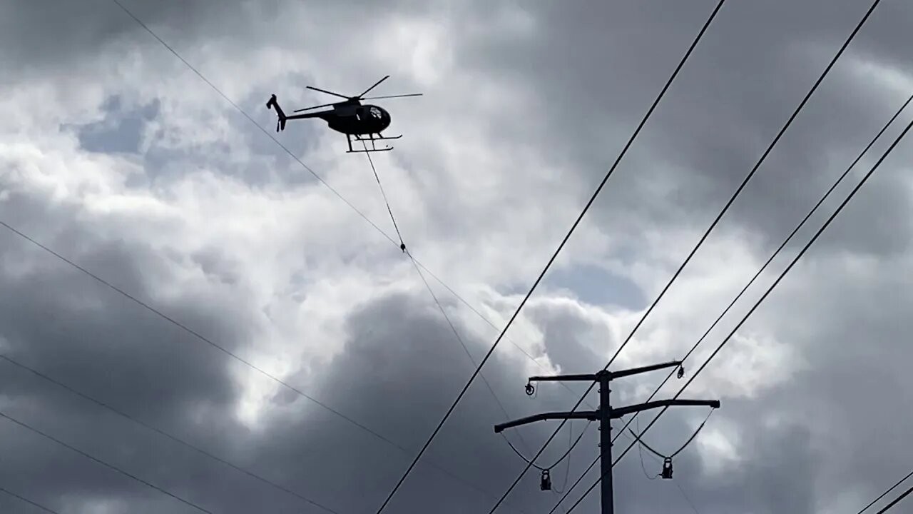 Helicopter running wire thru pulley on top of a huge high tension / high voltage lines tower