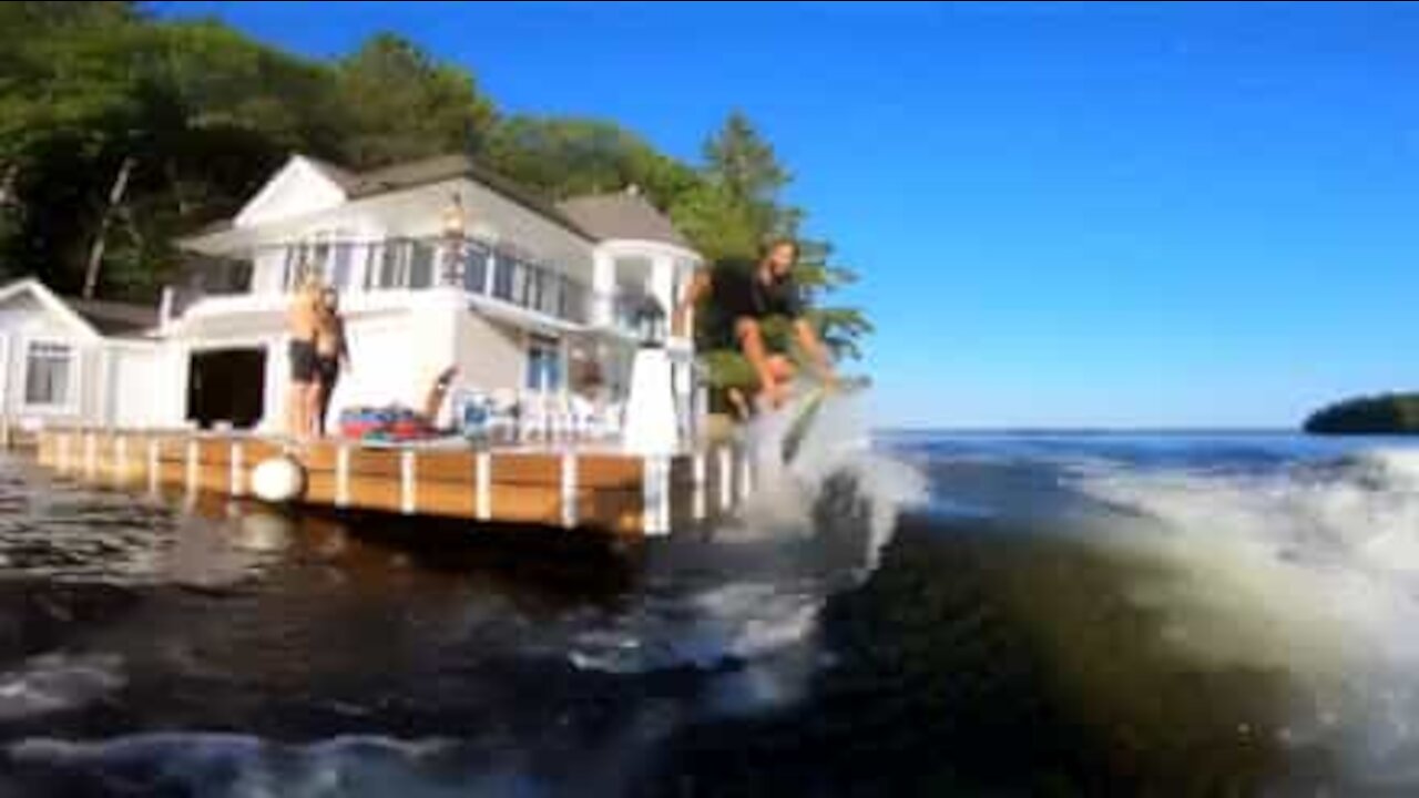 Raggiunge una barca cavalcandone l'onda con una tavola da surf