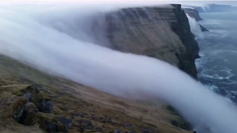 An ethereal waterfall created by a river of fog flowing over the cliffs of Látrabjarg