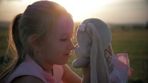 Little girl in pink festive dress holding big plush bunny toy at sunset. Silhouette of a child with