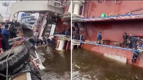 The ship capsized at the pier and is slowly sinking. People run away as horror can