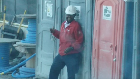 A Guy Blocks His Coworker From Exiting An Outhouse