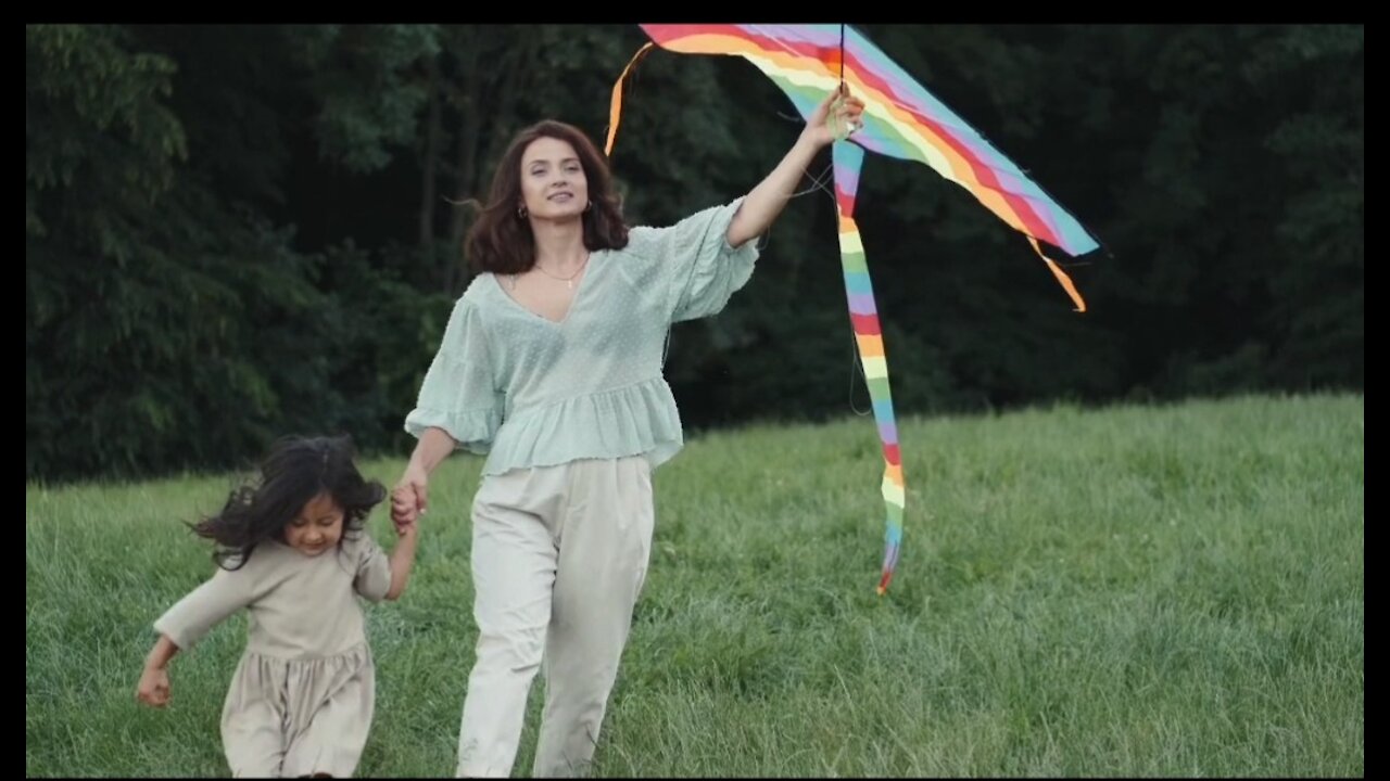 Mother and daughter walking in park with a big kite in hand