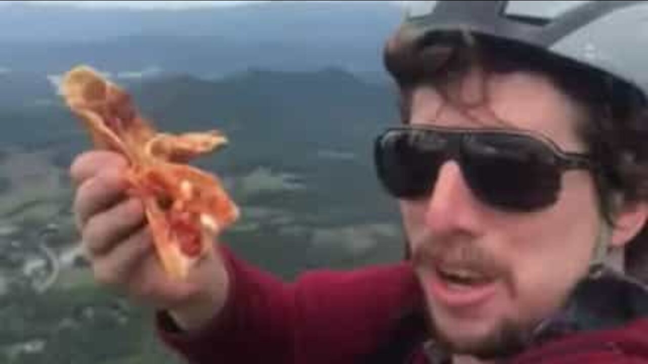 Amante de pizza come fatia enquanto faz parapente