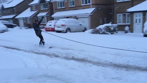 Dude snowboards from back of car through snowy streets