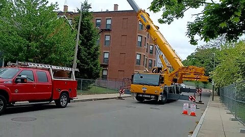 large crane lifting up antenna tower on roof