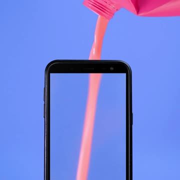 Cell phone filled with a pink liquid like a glass on a blue background