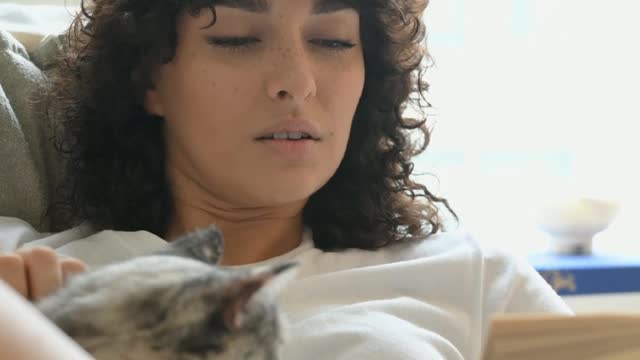 A woman reading a book while petting her cat