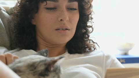 A woman reading a book while petting her cat