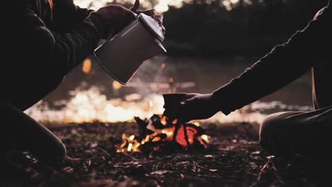 People pouring a warm drink around a campfire