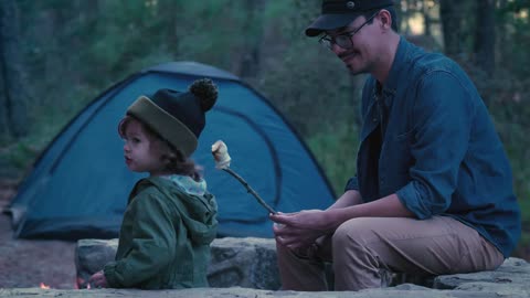 Young father giving roast marshmallow to his daughter outdoors