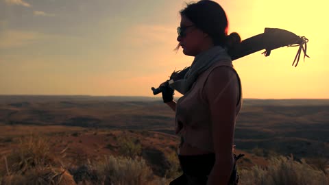 A woman walks on the edge of a hill with a weapon
