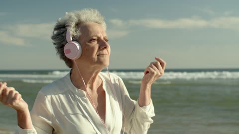 An elderly women dancing while using headphones at the beach