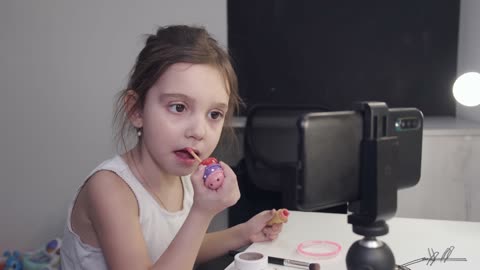 Little Girl Applying Lipstick While Looking At Her Smartphone