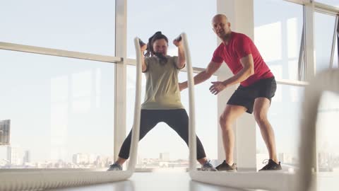 A Trainer Watching A Woman Do The Rope Smashing Exercise