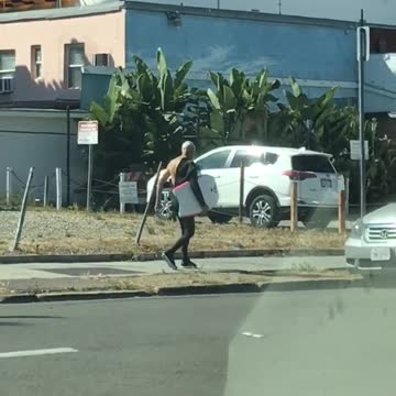 Old man with half a wet suit carrying yellow board