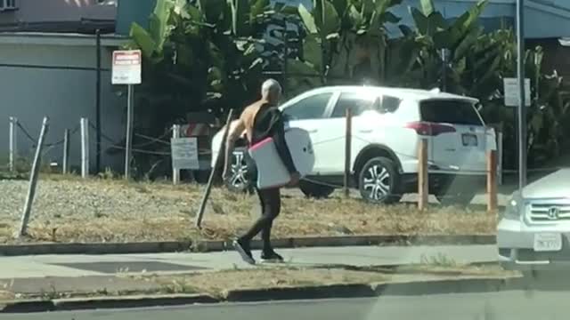 Old man with half a wet suit carrying yellow board