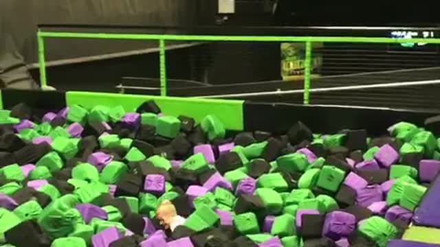 Little kid white shirt front flips into black purple green foam pit