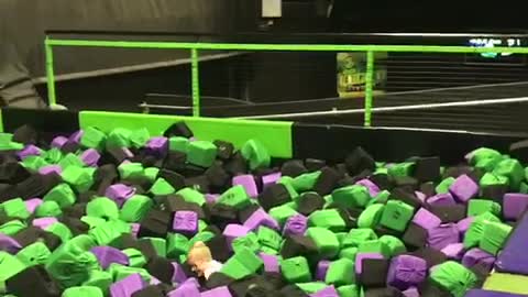 Little kid white shirt front flips into black purple green foam pit