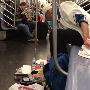 A man on a subway surrounded by his things on subway