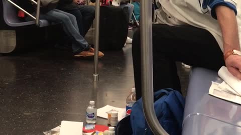 A man on a subway surrounded by his things on subway