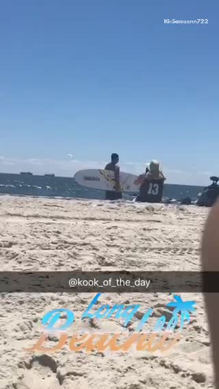 13 jersey guy taking picture of friend holding surfboard on beach