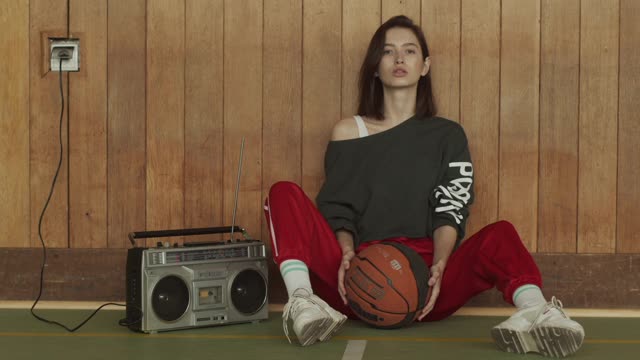 A Woman Sitting While Dribbling a Ball Beside a Radio