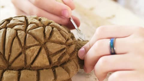 Child is scratching the texture of the scales on handmade turtle toy from clay