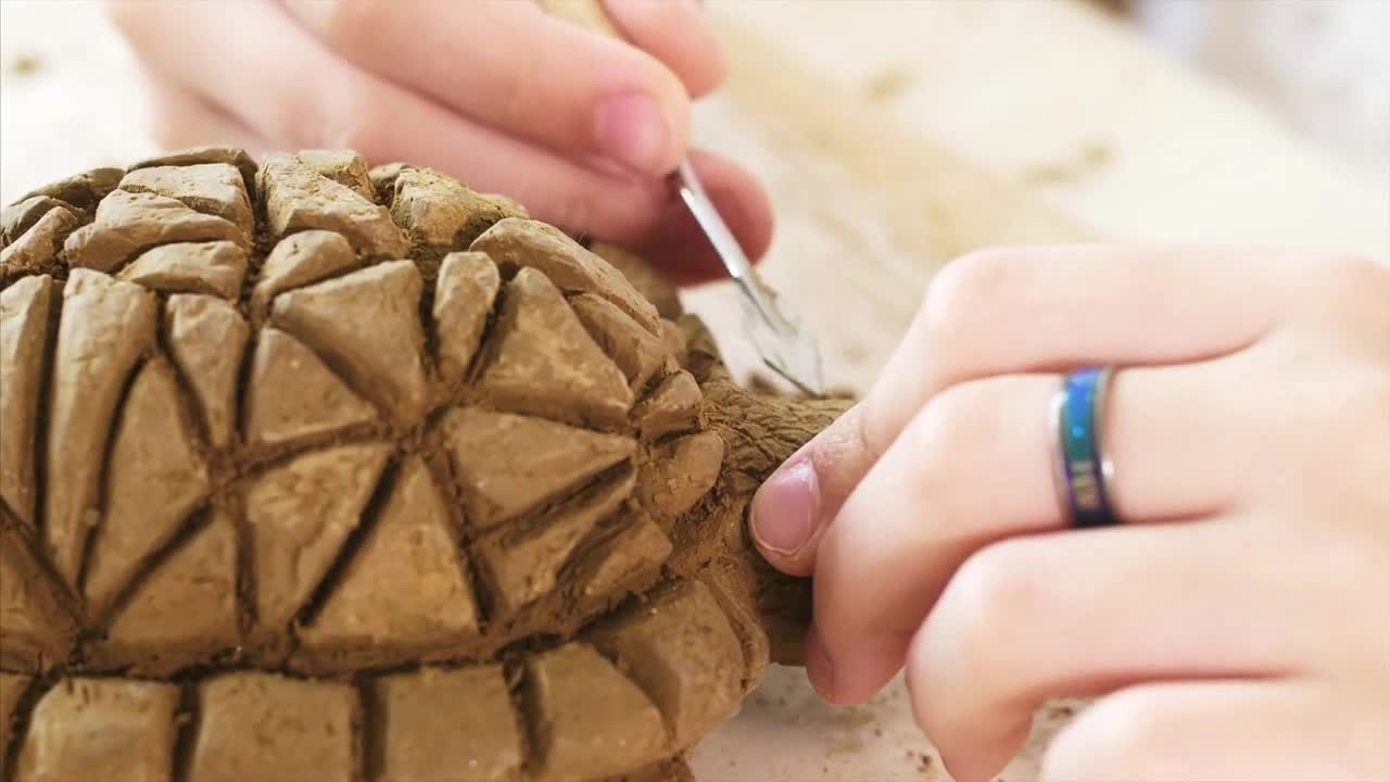 Child is scratching the texture of the scales on handmade turtle toy from clay