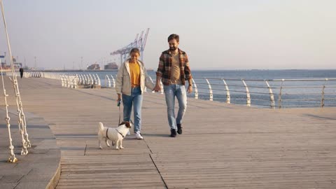 Cheerful young couple walking Jack Russel terrier dog outdoors near the sea