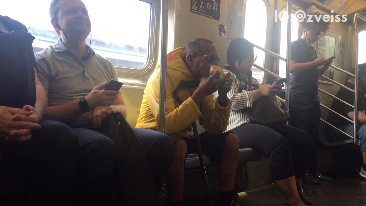 Man yellow jacket eating whole mango subway train