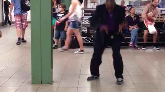 Man in black and purple suit dances crazily to a piano song in a subway station