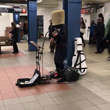 Man with basket on head plays guitar and sings on subway