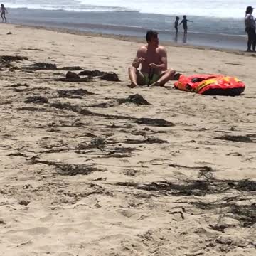 Man on beach next to orange raft has shake weight