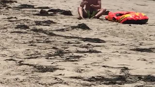 Man on beach next to orange raft has shake weight