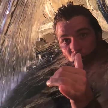 Guy swimming in water and opens mouth near waterwall