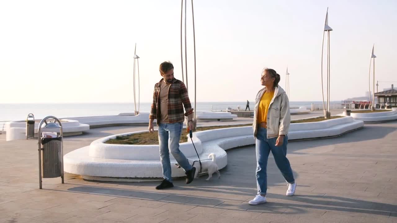 Cheerful young couple walking Jack Russel terrier dog outdoors near the sea