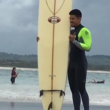 Guy in green wetsuit posing next to board