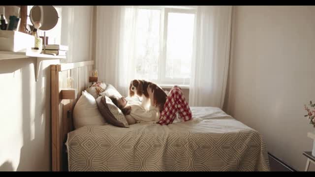 A cute young girl carries her spaniel dog around the room in her arms and lies down with