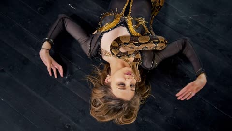 Beautiful woman lying on the floor with a snake dancing in a studio