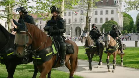Group of heavily equipped police officers ride horse through city park