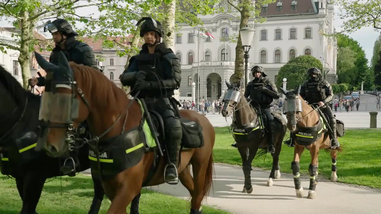 Group of heavily equipped police officers ride horse through city park